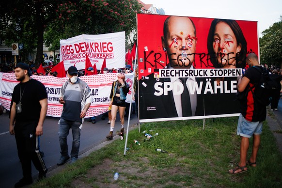 epa11313376 Protesters with a banner reading 'War to the war' pass by a Social Democrats campaign poster showing German Chancellor Olaf Scholz and Vice-President of the European Parliament a ...