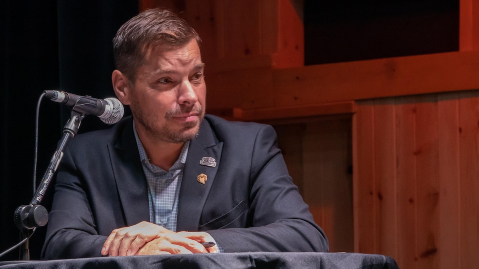  Guy Bernatchez assis &agrave; une table sur laquelle il y a un micro.